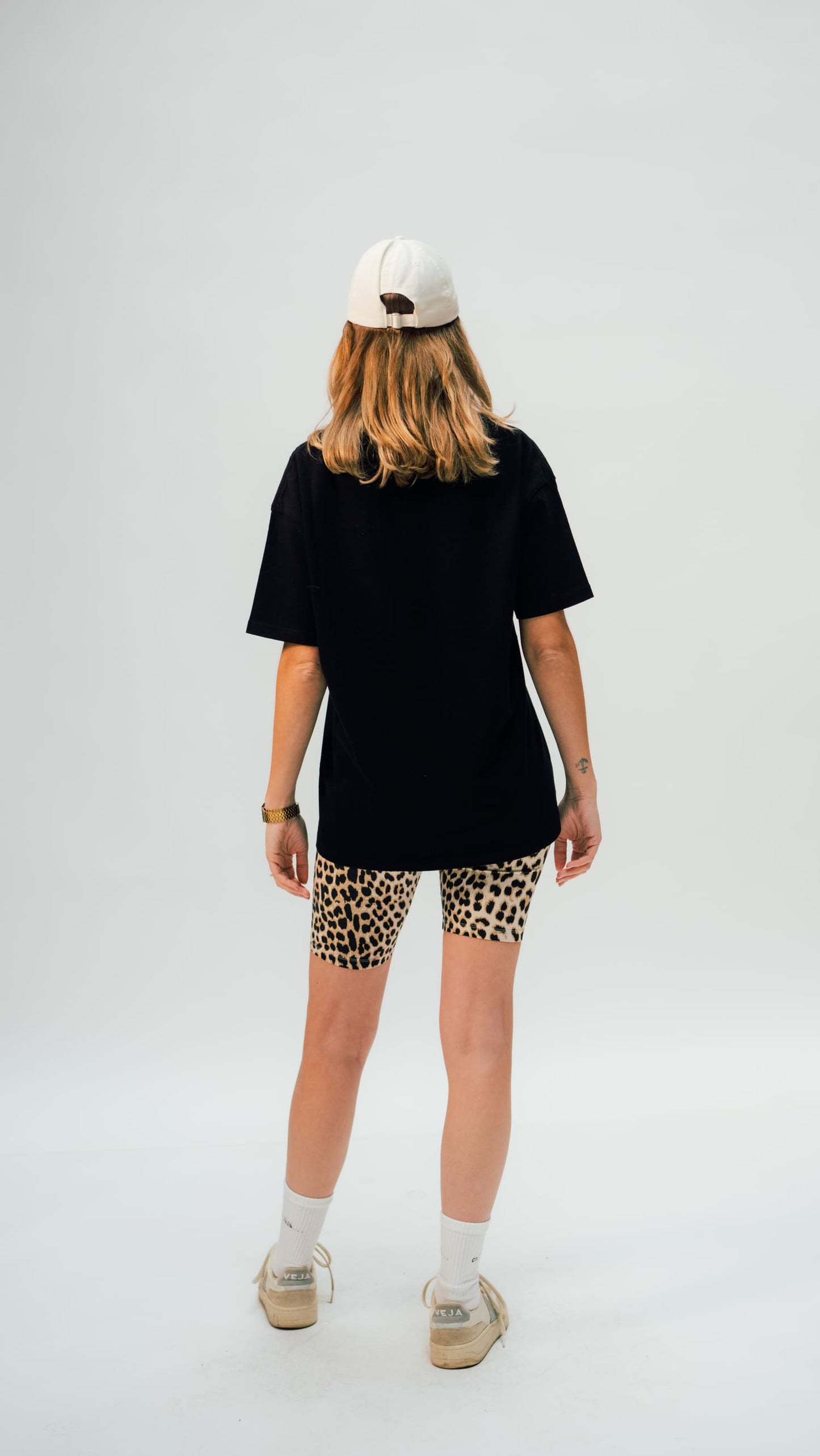schwarzes arrel unisex oversized t-shirt am weiblichen Model mit Cap von hinten