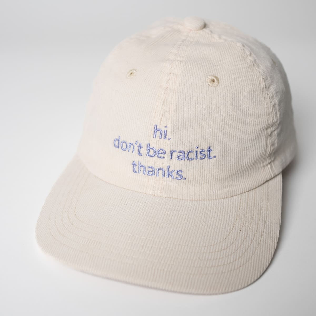 Nahaufnahme der hi. don't be racist. thanks. Cord Cap in beige mit Lavendel-farbener Schrift von arrel