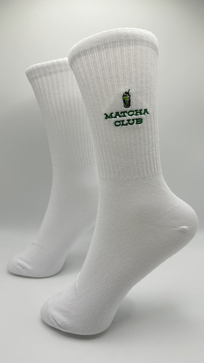 Matcha Club Statement Socken am Modell. Weiße Socke mit grüner Schrift und Matcha Glas von der Seite